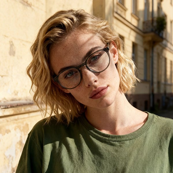 Junge Frau mit brauner Brille und grünem Oberteil im Sonnenlicht (KI-generiert).