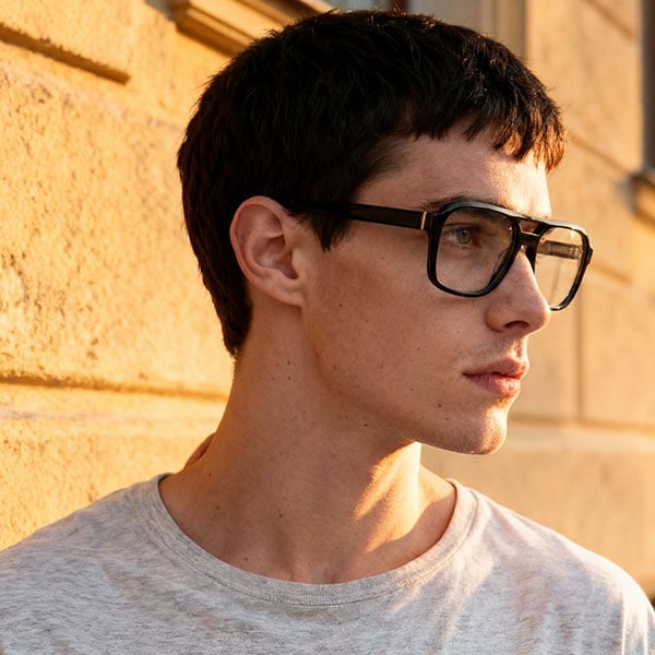 Mann mit kurzen dunklen Haaren und großer brauner Brille im warmen Sonnenlicht (KI-generiert).